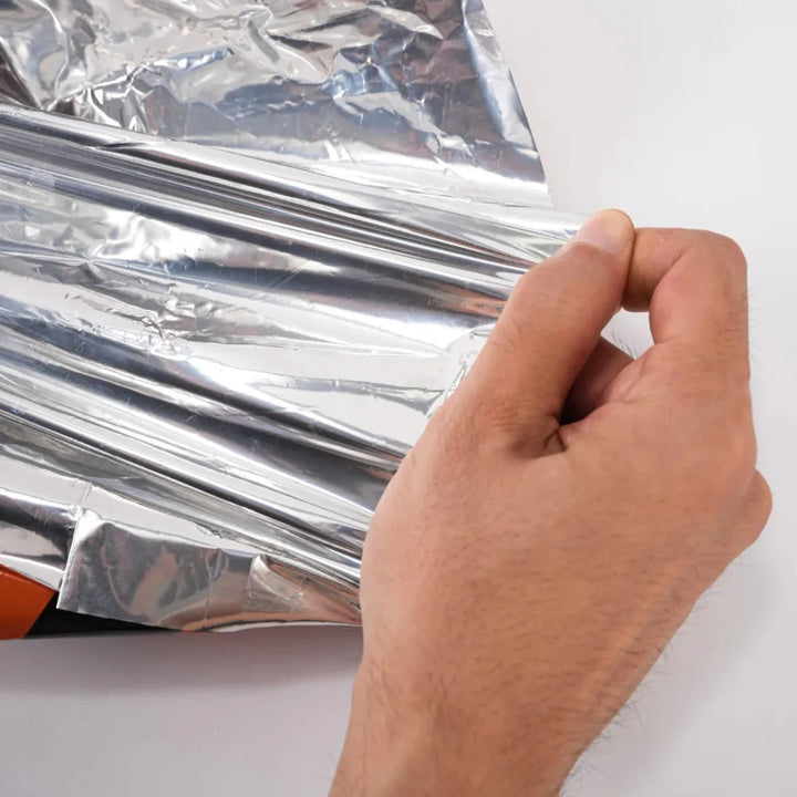 Hand holding a single emergency survival sleeping bag from the 4-pack, emphasizing its lightweight nature for hiking.