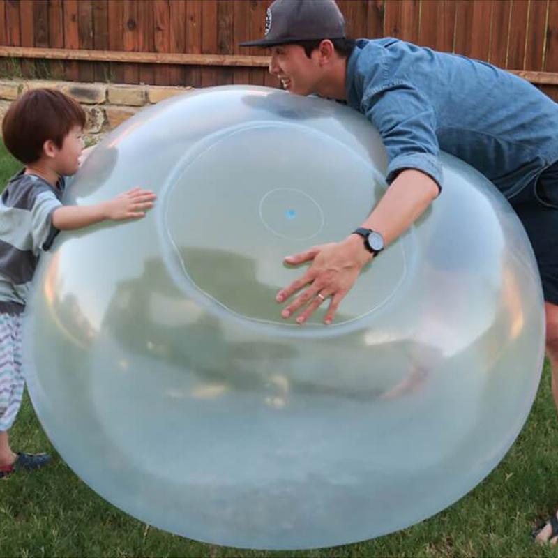 Kids playing with a giant inflatable bubble ball in the yard.