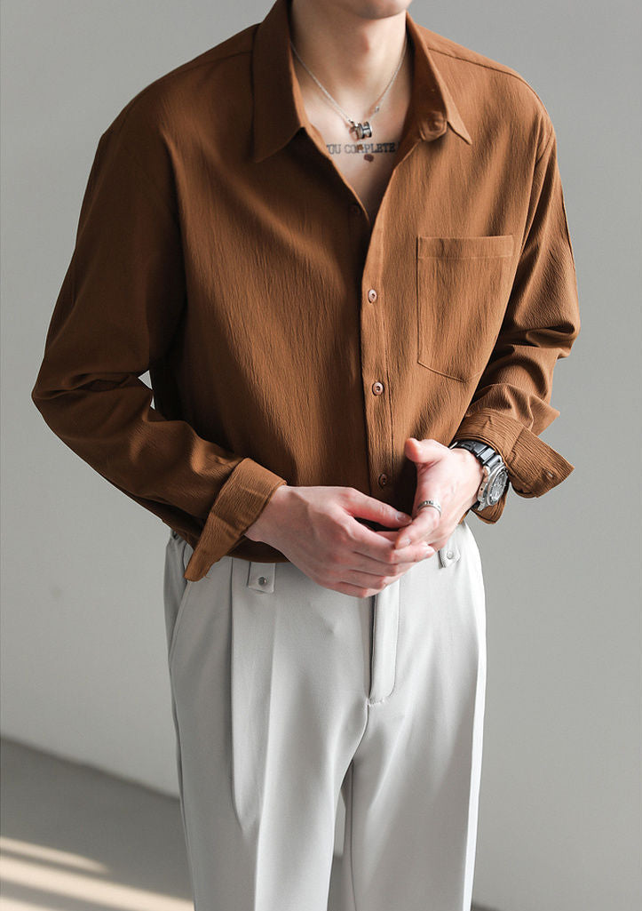 Stack of men's relaxed fit button-up shirts in brown, blue, white & black, showcasing versatile options.