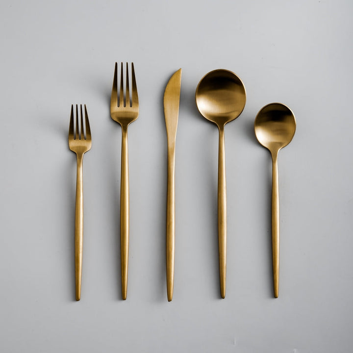 Modern minimalist matte gold flatware set elegantly arranged on a dining table.