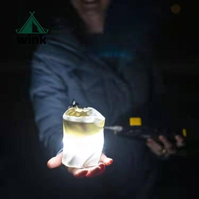 Portable inflatable LED camping lantern, magnetic, deflated, showing compact travel size and light.