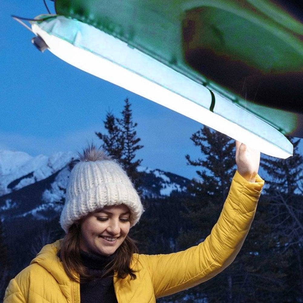 Portable LED light with magnetic base, shown illuminating a camp table with outdoor gear at night.