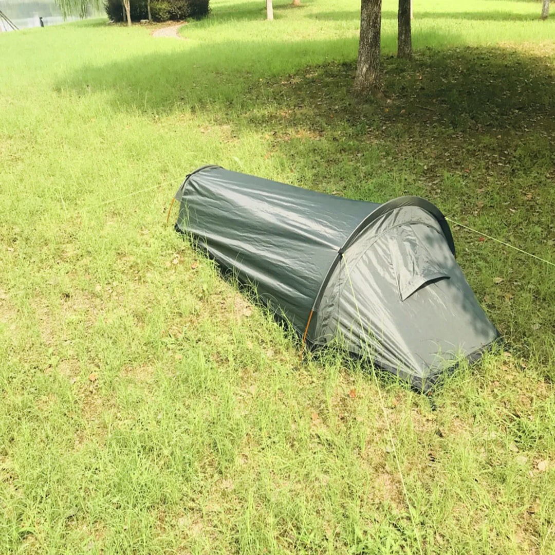 Lightweight bivy tent next to a backpack, illustrating its portability for hiking.