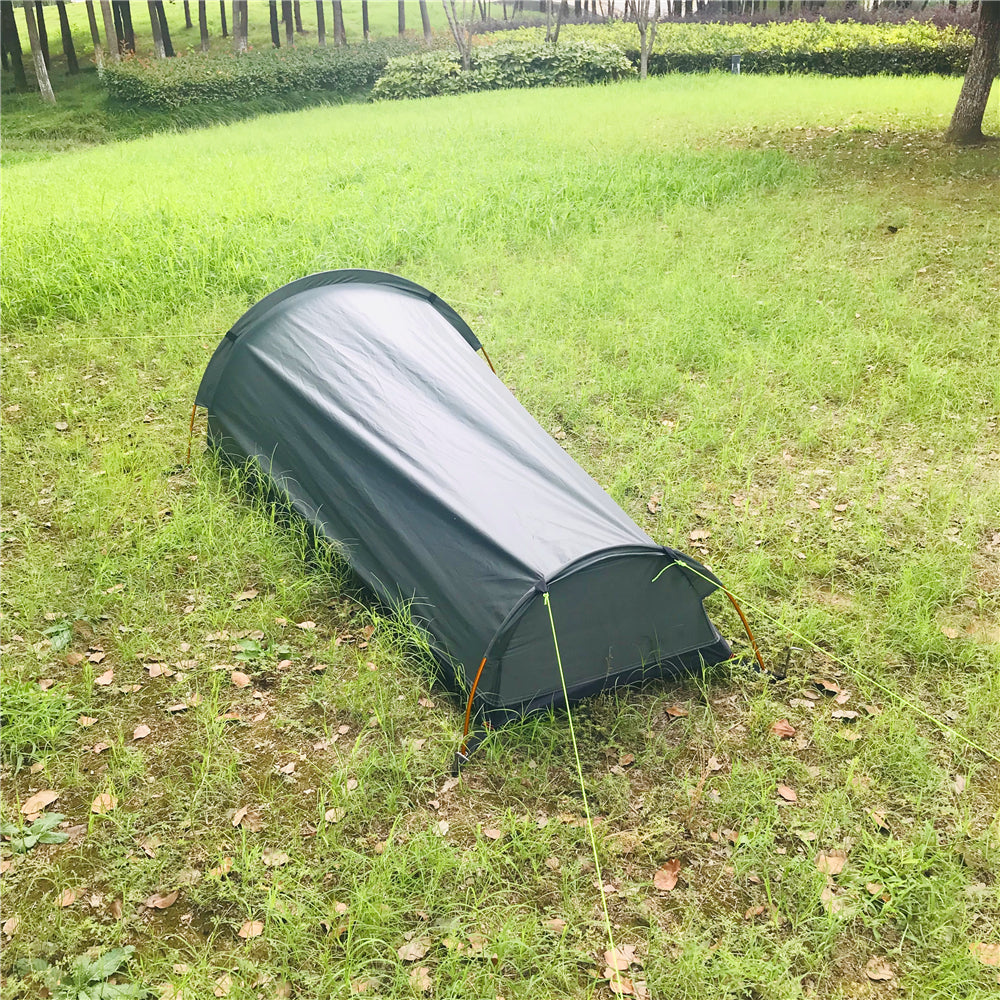 Survival shelter bivy tent, camouflaged in a natural outdoor environment.