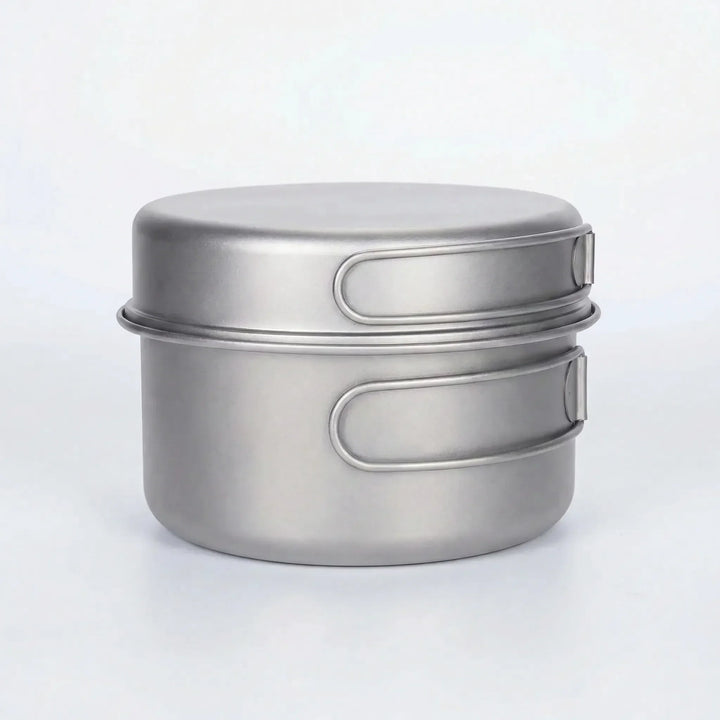 Portable titanium pot & pan set with folding handles, ideal for hiking & outdoor cooking.