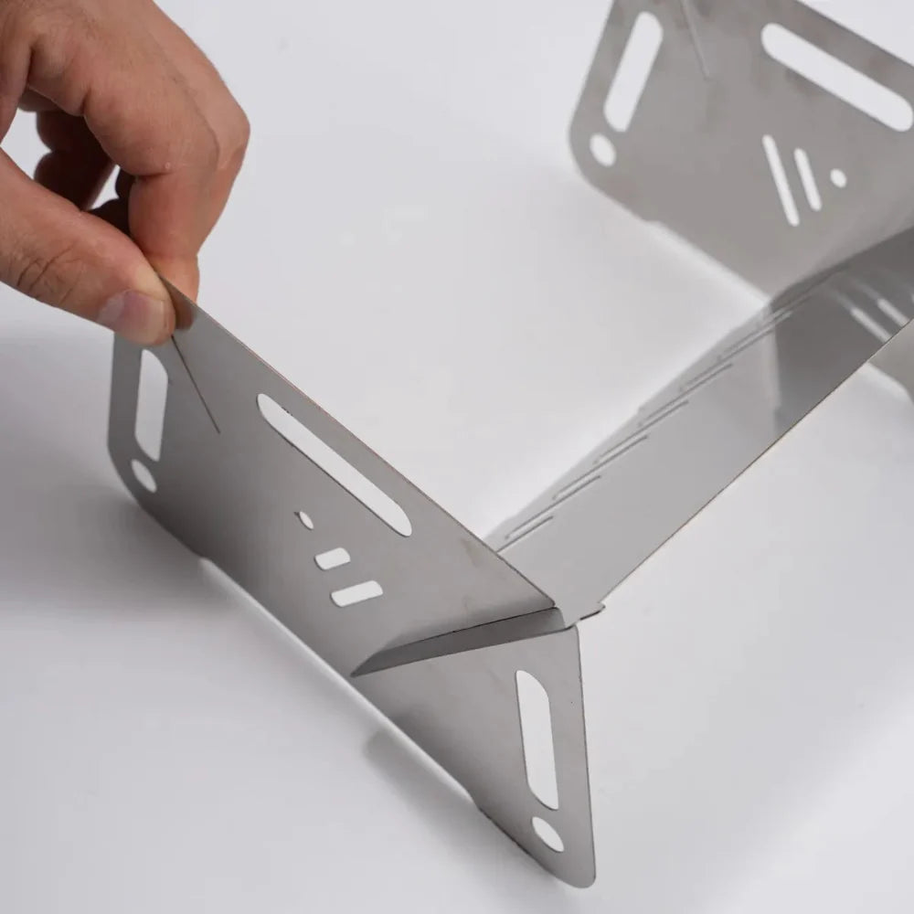 Compact stainless steel camping grill with burning coals, ideal for outdoor cooking and survival.