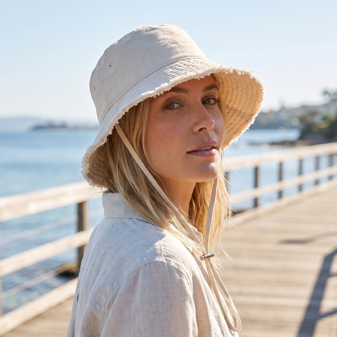 Women's distressed denim bucket hat with frayed brim & adjustable chin strap for summer beach style.